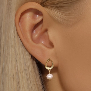 Close-up of golden irregular hoop earring with elegant pink pearl charm on model