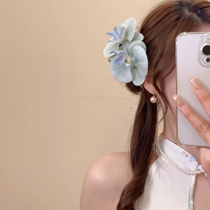 Detail of blue gradient floral hair clip and round pearl earrings on elegant model