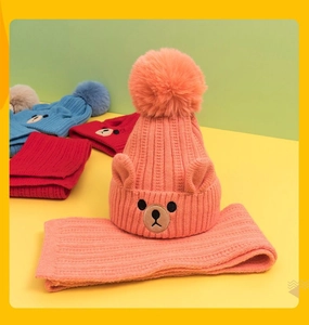 Detail of knit baby beanie and scarf set with cute bear embroidery and large pompom decoration