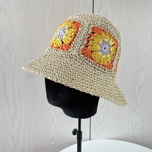 Detail of handmade crochet straw bucket hat with colorful flower patterns on a stand