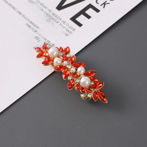 Detailed shot of golden leaf hair clip with sparkling red rhinestones and white pearls