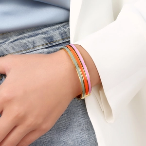 Detail showing stacked gold-plated enamel bangles in grey, orange, and pink on wrist