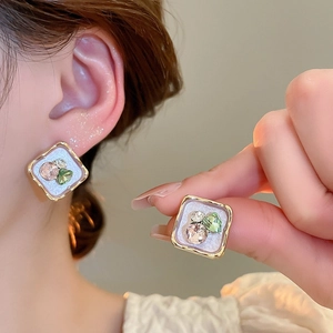 Detail of square gold-framed floral earrings with pink and green gems on model