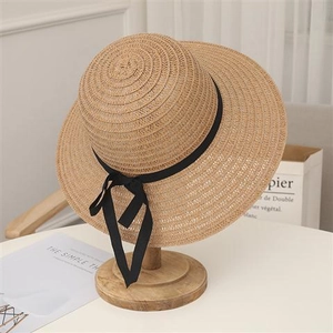 Dettaglio di un cappello di paglia a tesa larga con fiocco nero su supporto in legno