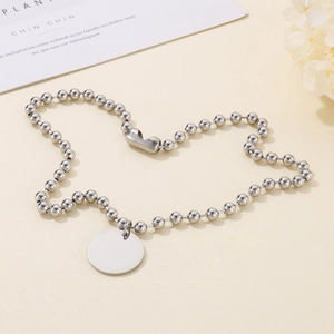 Détail d'un pendentif rond argenté poli monté sur une chaîne à billes classique