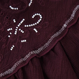 Close-up of wine red textured shirt featuring white bead embroidery and zigzag stitching