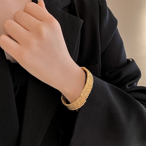 Detail of layered gold-plated textured bangle on model with elegant black suit