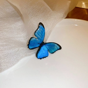 Detail showing gradient blue butterfly brooch with glitter finish on white pedestal