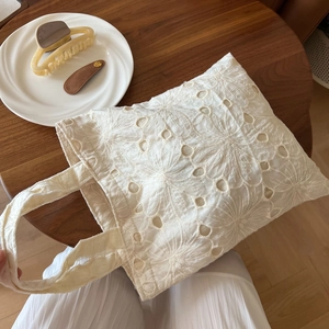Detailed shot of white lace embroidery tote bag on a dark wooden table with soft lighting