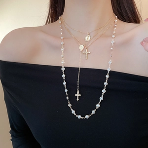 Detailed view of layered gold cross necklace with pearls and religious icons on model