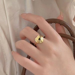 Detail of a minimalist gold wavy ring with black heart inlay worn on person