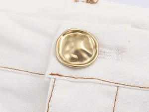 Detail of vintage gold button and brown contrast stitching on white flared pants