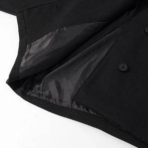 Gros plan du manteau en laine noire montrant la texture du tissu, la doublure et le bouton