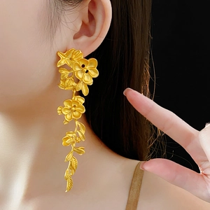 Détail de boucles d'oreilles pendantes fleurs et feuilles dorées au fini mat brossé