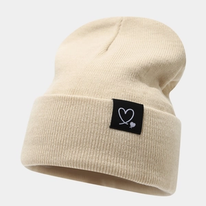 Gros plan d'un bonnet en maille beige avec un écusson cœur noir et une texture côtelée