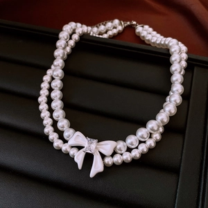 Detail showing double-layer pearl necklace with a white bow and square gemstone inlay