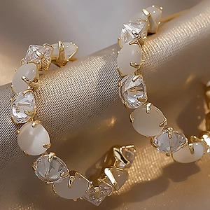 Detail of gold-plated C-shaped earrings with faux cat-eye stones and cubic zirconia