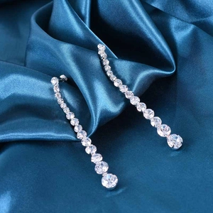 Macro shot of 925 silver needle drop earrings with sparkling crystals on blue silk