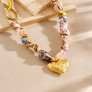 Close-up of gold wrinkled heart pendant with chain print silk scarf ribbon necklace