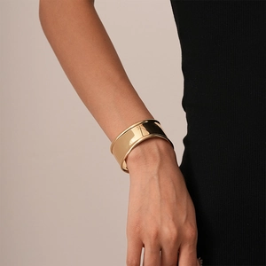 Detailed view of wide polished gold metal cuff bracelet on woman's wrist
