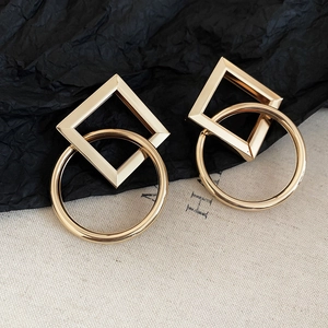 Macro view of interlocking gold geometric round and rhombus metal earrings on textured fabric
