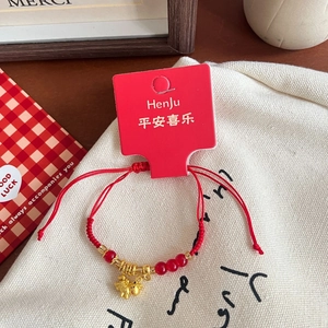 Detail of red woven bracelet with a golden pig charm and brand tag on canvas background