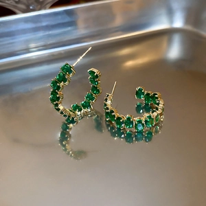 Dettaglio di orecchini a cerchio dorati a forma di C con vivaci pietre verde smeraldo