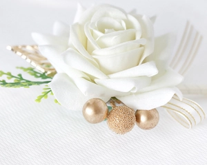 Close-up of white artificial rose boutonniere with gold leaves and ribbon for weddings