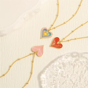 Rainbow heart pendant necklaces in red and pink with gold beaded chains on textured base
