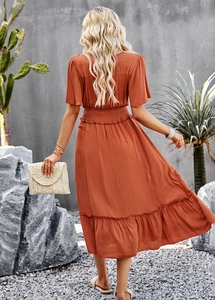Back view of orange V-neck maxi dress with elastic waist and ruffled detail in a garden