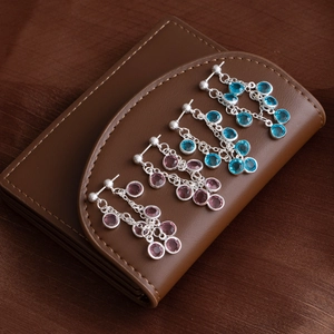 Elegant silver tassel earrings with pink and blue gemstones on a brown leather wallet
