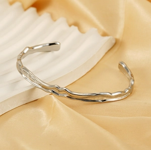 Detail of silver hammered texture cuff bracelet on white stone and gold silk fabric