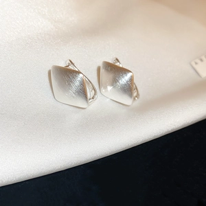 Macro view of silver U-shaped earrings with brushed metal finish on silk background
