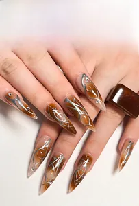 Détail macro de faux ongles stiletto ambre avec lignes argentées et strass brillants