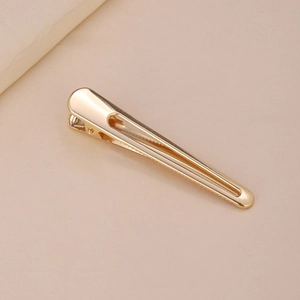 Close-up of golden minimalist metal duckbill hair clip with polished finish surface