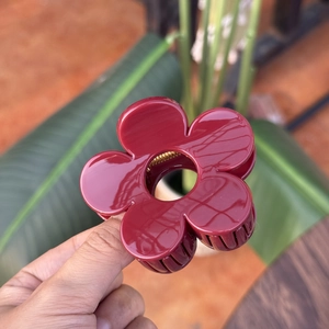 Détail d'une pince à cheveux fleur rouge foncé brillante de 8 cm tenue à la main
