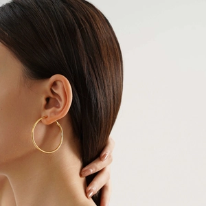 Close-up of model wearing large minimalist golden stainless steel hoop earrings