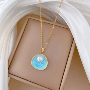 Collier en titane doré avec pendentif en émail bleu et perle sur un écrin à bijoux beige