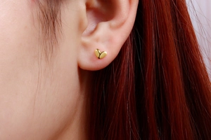 Close-up of small golden heart screw back earring on earlobe with polished finish