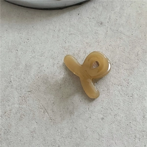 Detailed close-up of a cream-colored acetate mini hair claw clip on a textured surface