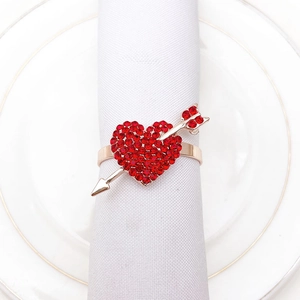 Detail of a gold heart napkin ring with red rhinestones and arrow on a white napkin
