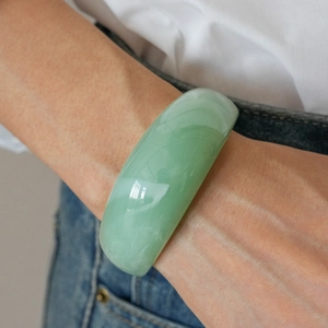 Close-up of a wide translucent light green resin bangle with smooth polished finish
