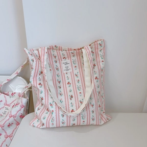 Detail of floral canvas tote bag featuring red flower prints and vertical stripes with a woven label