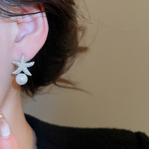 Gros plan sur des boucles d'oreilles étoile de mer avec zircons et perle blanche sur l'oreille