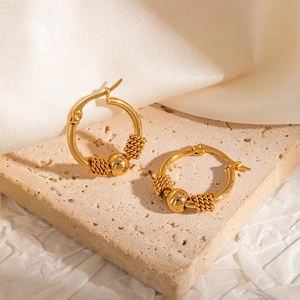 Detail of 18k gold plated hoop earrings with textured beads on a stone background