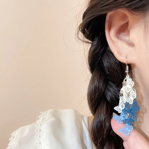 Dettaglio di lunghi orecchini a farfalla con nappe blu sfumate su modella donna