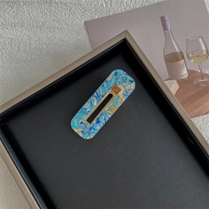 Detailed macro of a rectangular blue and white marble hair clip on a black tray