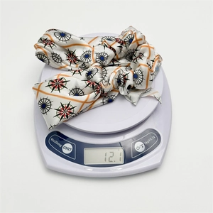 Detailed close-up of a floral silk scrunchie weighing 12.1g on a digital scale