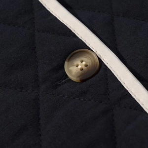 Close-up of black diamond quilted jacket fabric with beige trim and 4-hole button detail