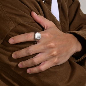 Silver octagonal signet ring for men on hand with a textured brown jacket background